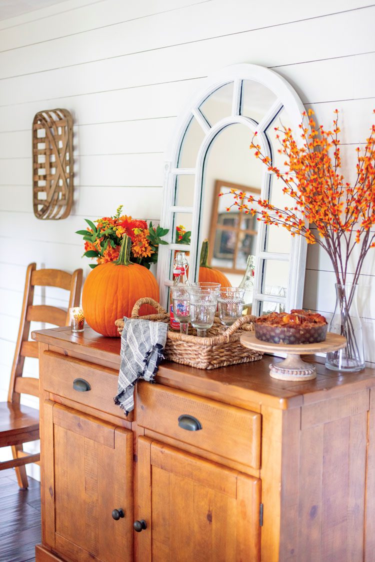 Nina's dresser has a white-paneled mirror leaning against the wall with pops of orange in fresh and artificial foliage with a plump pumpkin.