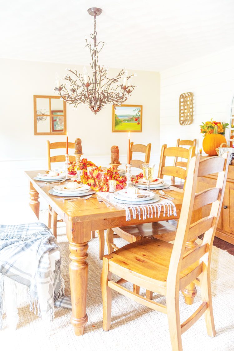 Nina's dining room has a simple wood table with wood chairs to complement her gorgeous and intricate chandelier that looks like fall branches hanging over the table runner.