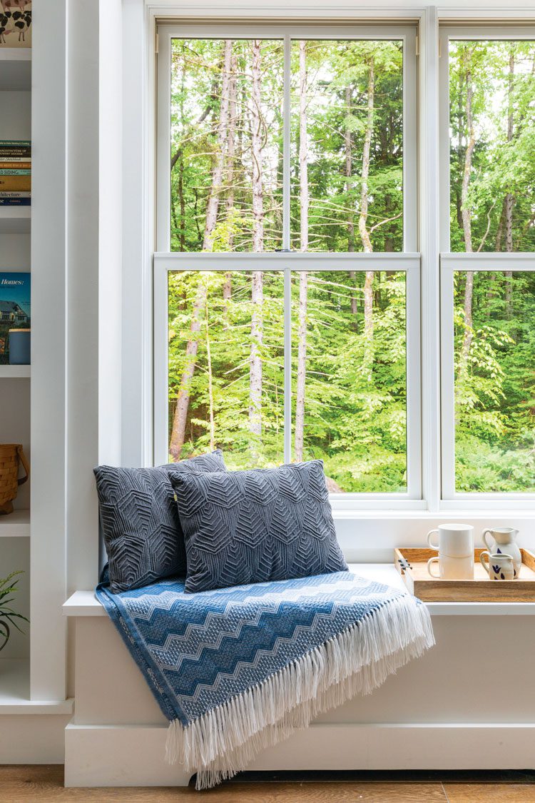 The window seat in this farm-cottage bedroom showcases a beautiful view of bright green forest land, plus double hung windows for farmhouse style