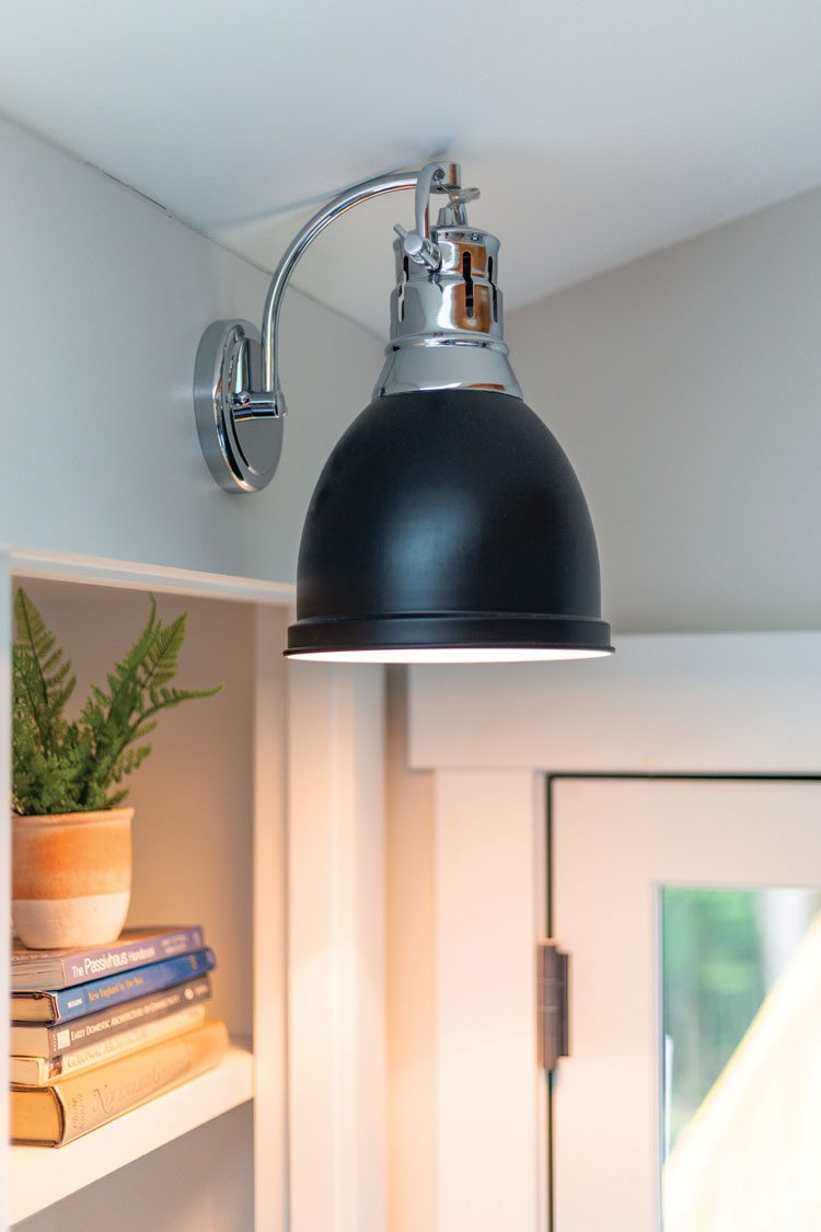 The wall light in this farm-cottage bedroom has a black dome shade with a silver neck.