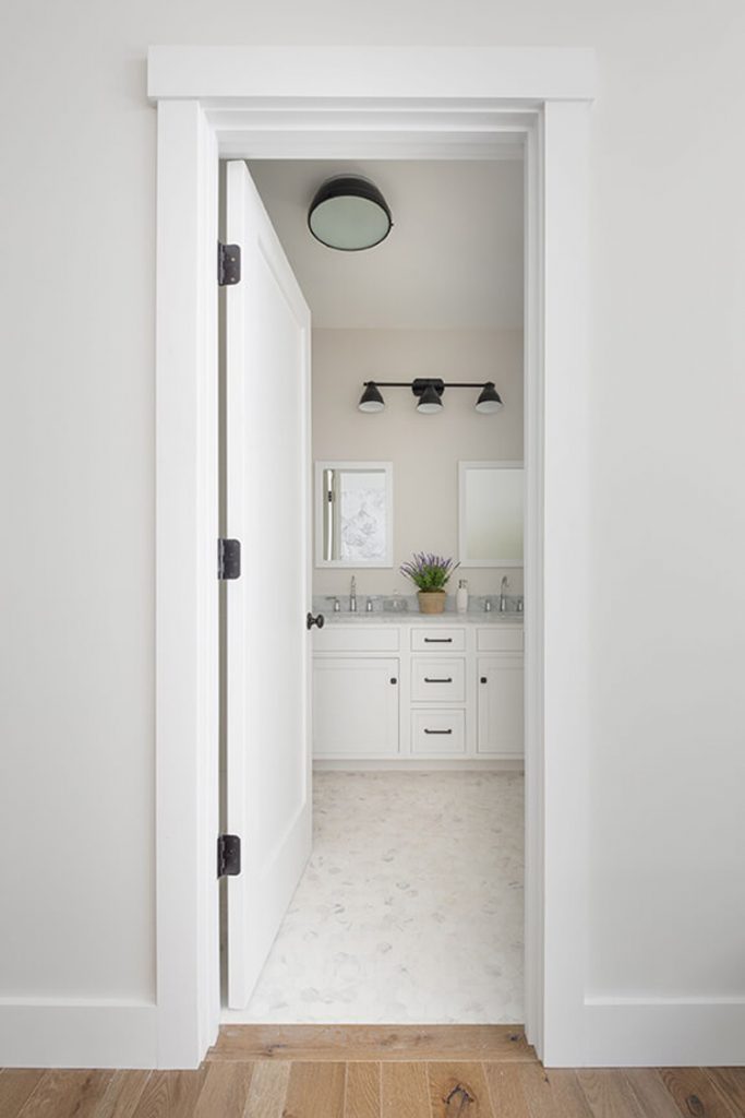 This bathroom shows how to match white paint with off-white paint. It has a white door and white cabinets with off-white flooring and walls.