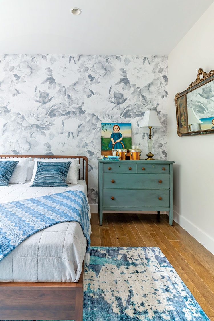 This farm-cottage bedroom has a mottled blue and white rug with a solid sea-foam-colored dresser next to the bed.