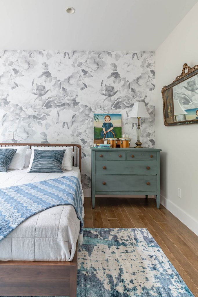 Large queen bed in a room with white and blue wallpaper and other details.