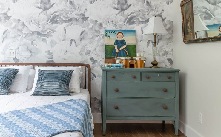 Large queen bed in a room with white and blue wallpaper and other details.