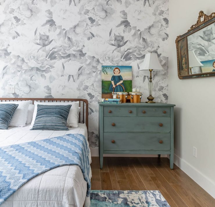 Large queen bed in a room with white and blue wallpaper and other details.