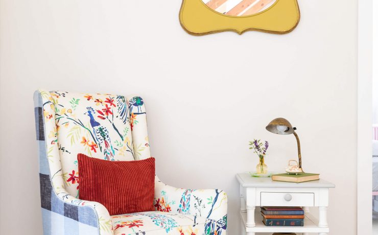A colorful gingham and floral patterned arm-chair with a white side table in front of a white paint wall.