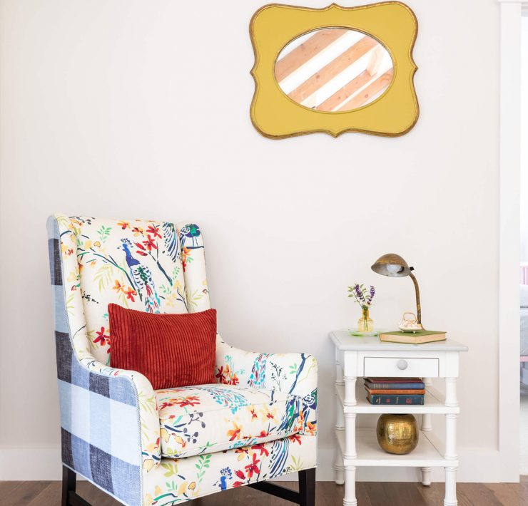 A colorful gingham and floral patterned arm-chair with a white side table in front of a white paint wall.
