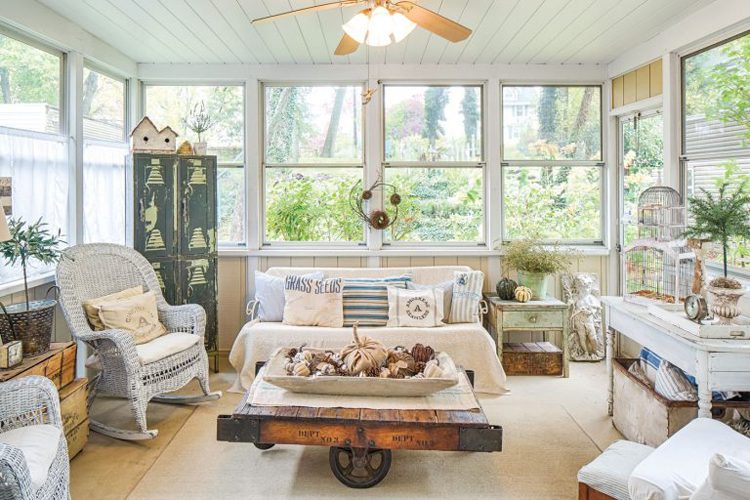 This flea-market inspired room shows how to decorate with lots of rustic furniture. It has a comfy sofa at the far end with two white, wicker chairs facing towards a coffee table made out of rustic wood.