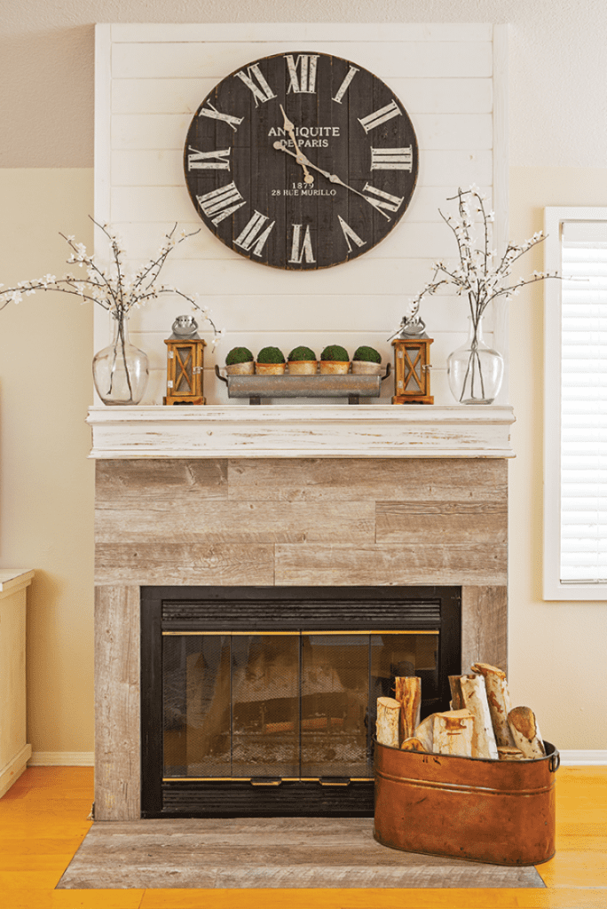 This fireplace mantel is decorated with faux plants, wood lanterns and a giant vintage clock. A perfect example of how to decorate with what you already have.