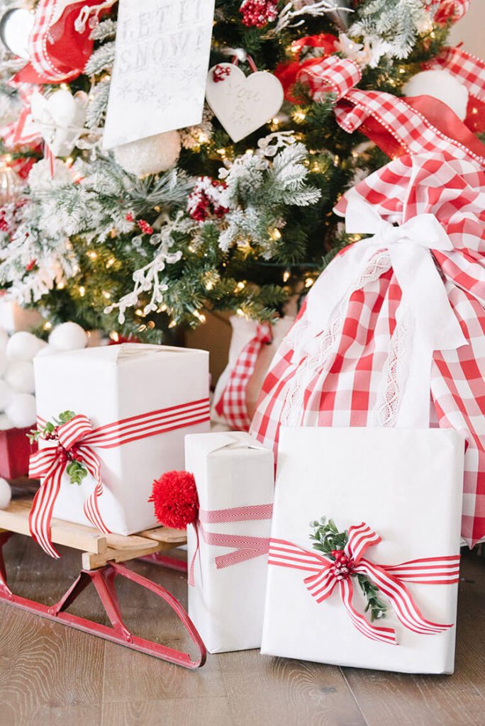 White gift wrap on packages with red embellishments under a Christmas tree