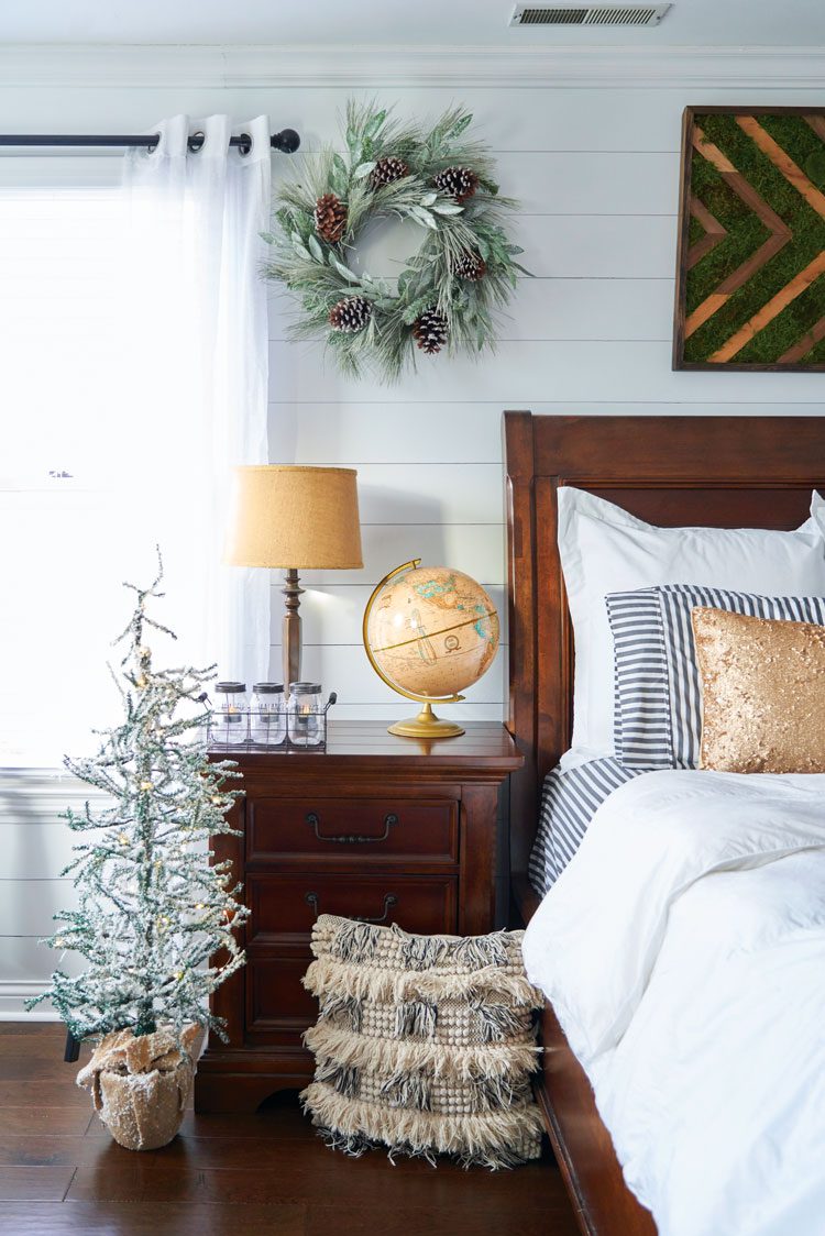 The master bedroom includes artificial greenery, dark wood furniture and gold accents in the pillows, table lamp and globe.