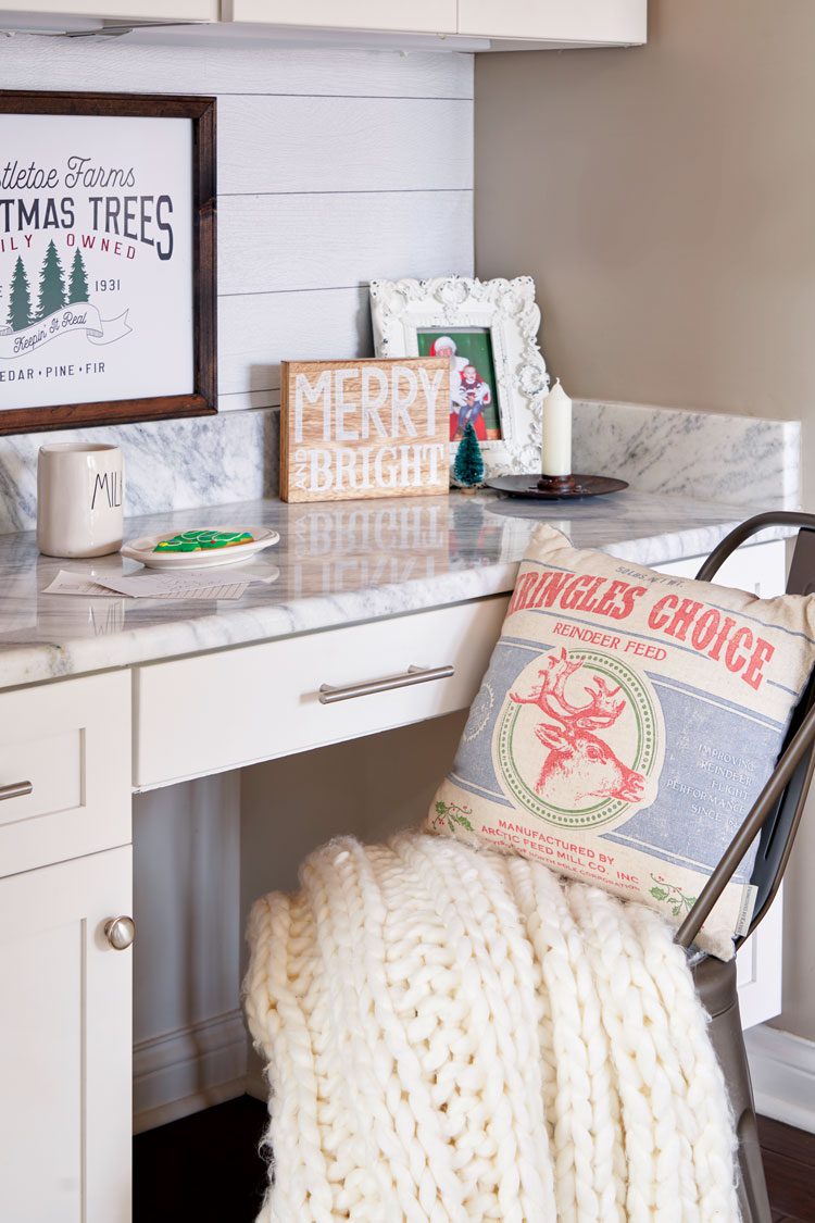 A workspace desk and a chair with a heavy cream knitted blanket and red and blue grain-sack inspired pillow.