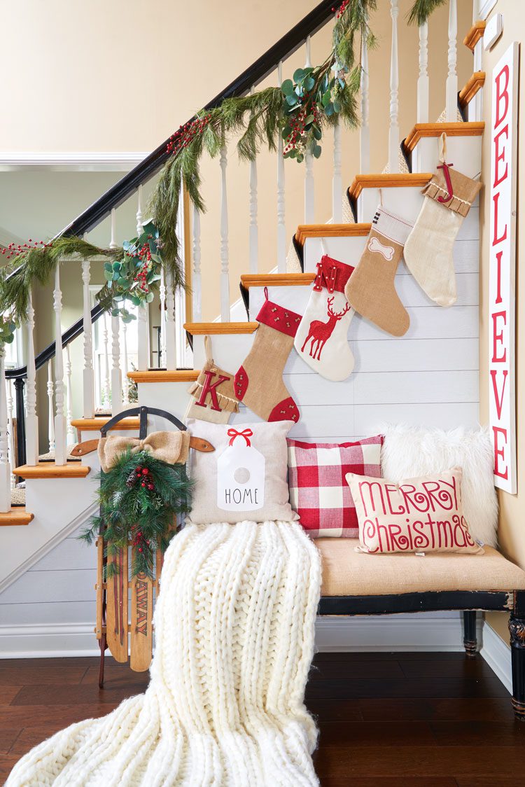 A bench with blankets and pillows beneath the garland-warped banister of their family friendly Christmas house.