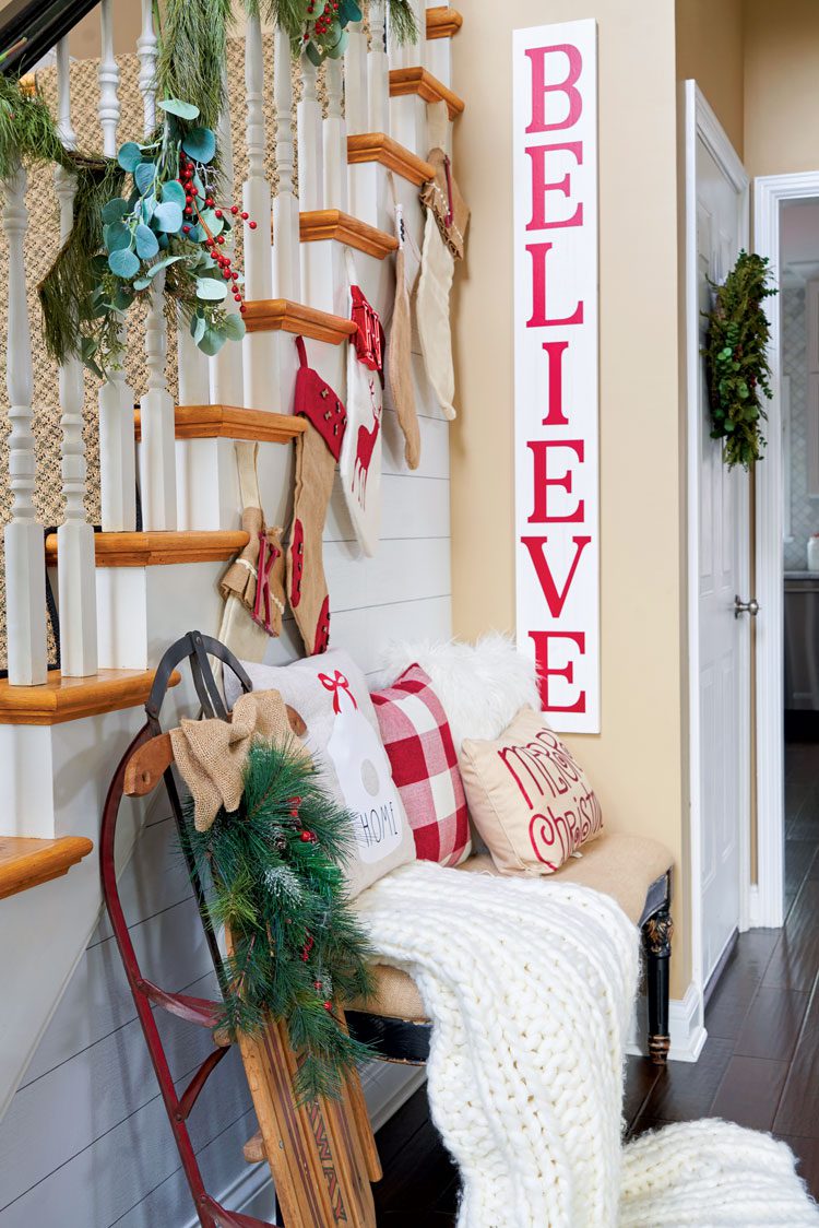 A small strip of wall is decorated with a white and red "believe" sign below the banister in their family friendly Christmas house.