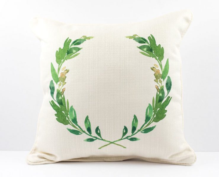 Cream-colored pillow with a watercolor green laurel wreath printed on it.