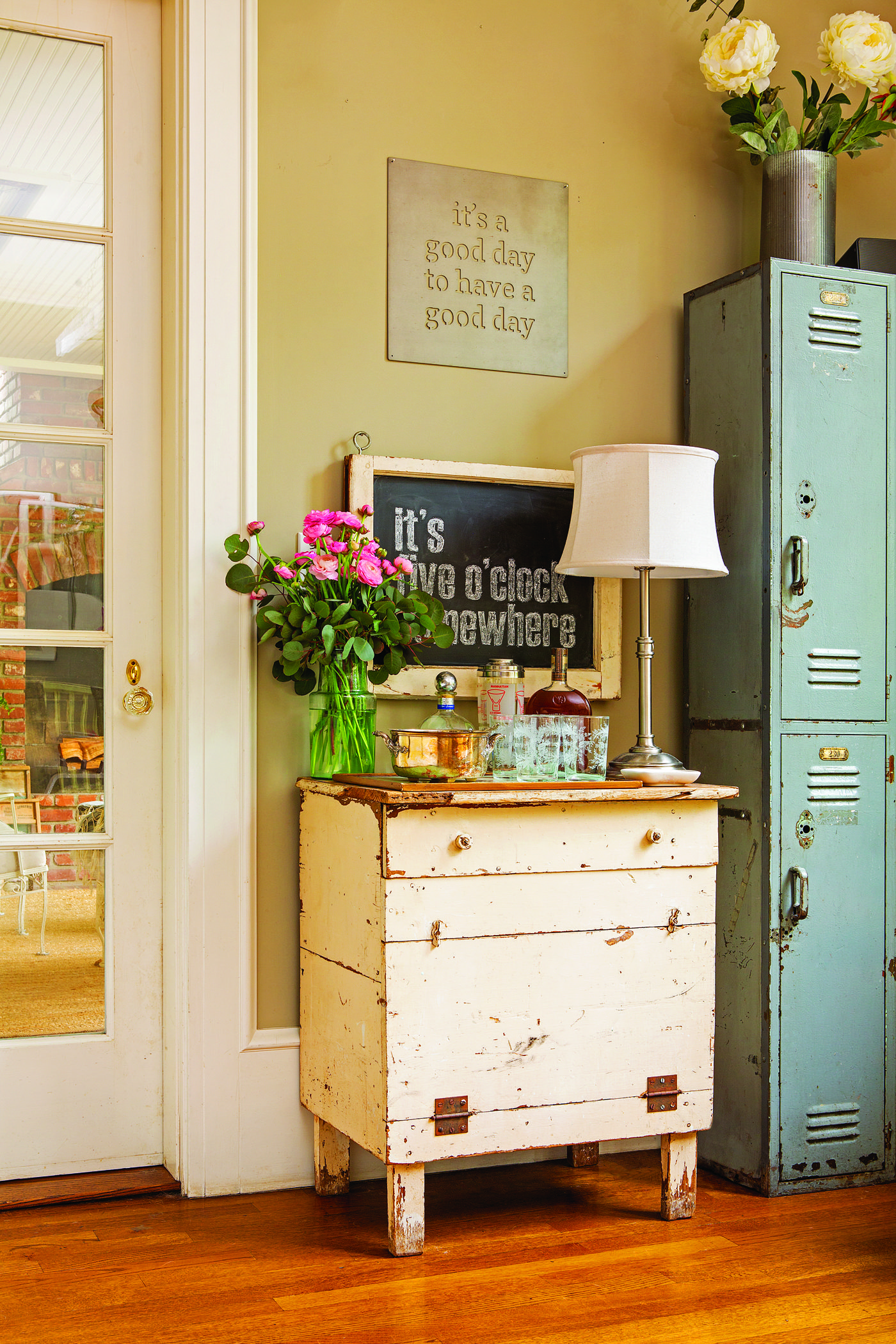 A cream-colored vintage desk with a lamp, bouquet of flowers and teal vintage lockers next to it demonstrates how to decorate with what you already have.