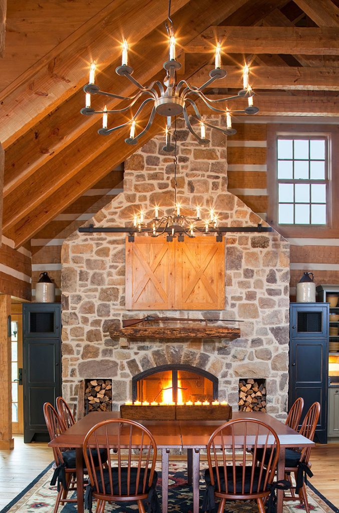 A wooden table sits before a vast stone chimney. 