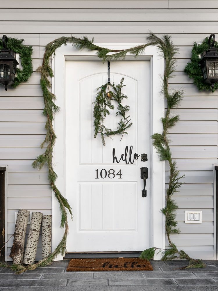 The white front door of the white Christmas home decorated with a thin garland and wreath.