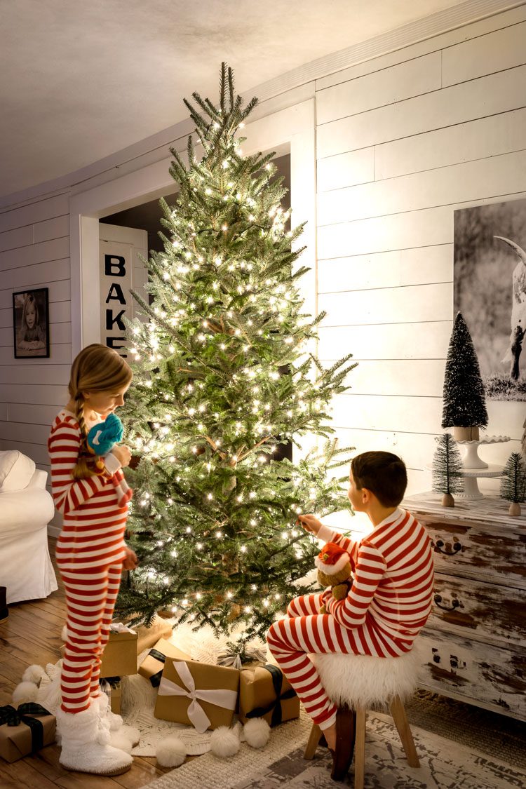 Two children beside the glowing Christmas tree in red and white striped pajamas.