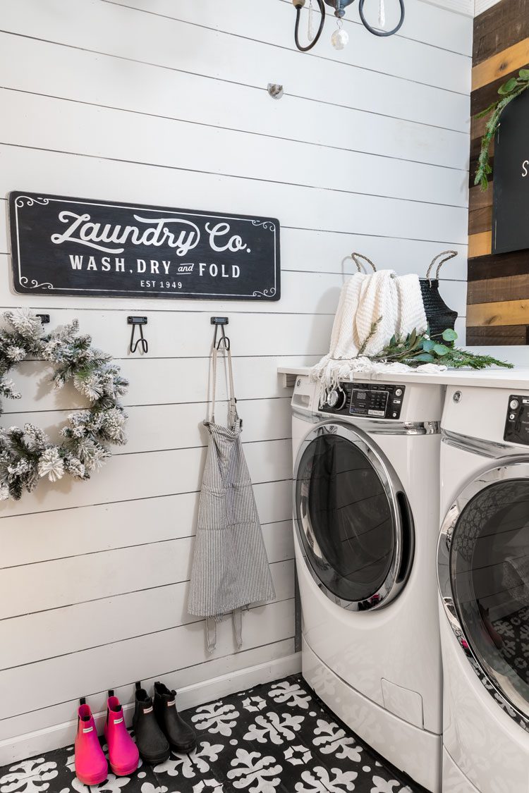 Laundry room of the white Christmas home with white shiplap walls and hand-painted black and white patterned tile flooring.