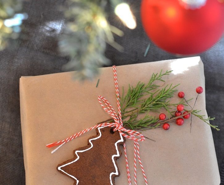 Christmas present wrapped in brown paper packaging with a cinnamon gingerbread Christmas tree ornament attached to it with string.