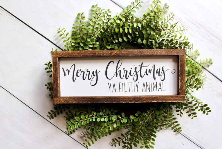 A wood framed, rectangular sign that says "Merry Christmas Ya Filthy Animal" in mixed black fonts on a white background.