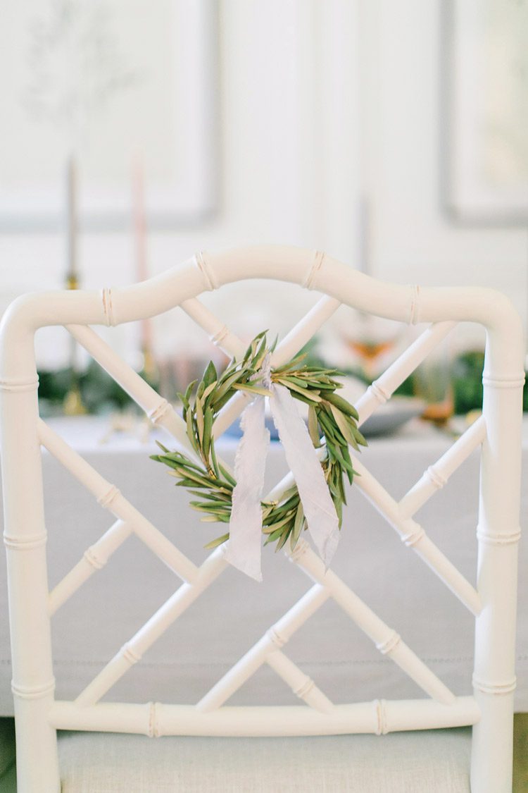 A small green wreath adorned with a white ribbon hangs off the back of each chair.