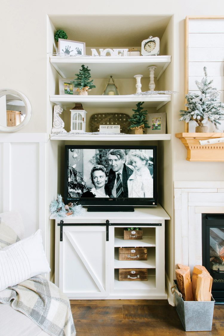 Small, white media table with sliding barn door holding up a TV with "It's a Wonderful Life" scene on the screen.