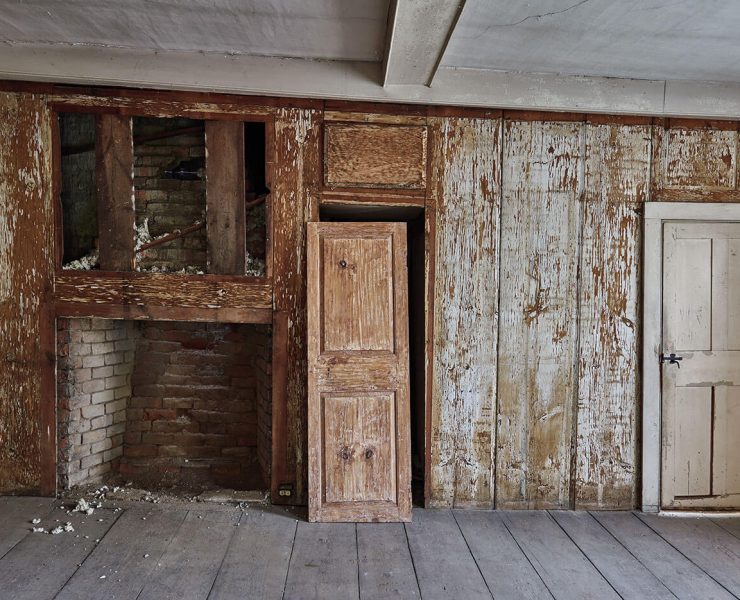 A room made of old wood waiting to be reclaimed. In the center, an antique door leans against its frame.