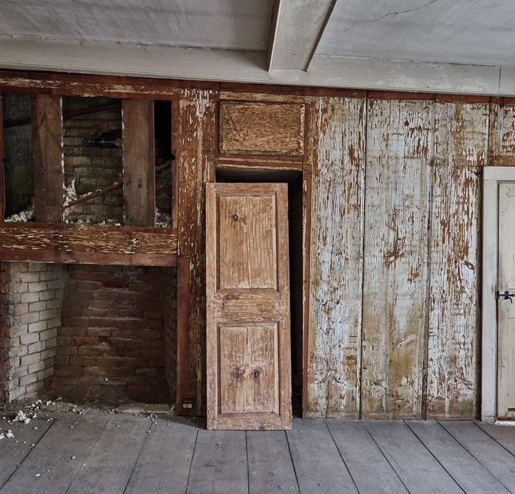A room made of old wood waiting to be reclaimed. In the center, an antique door leans against its frame.