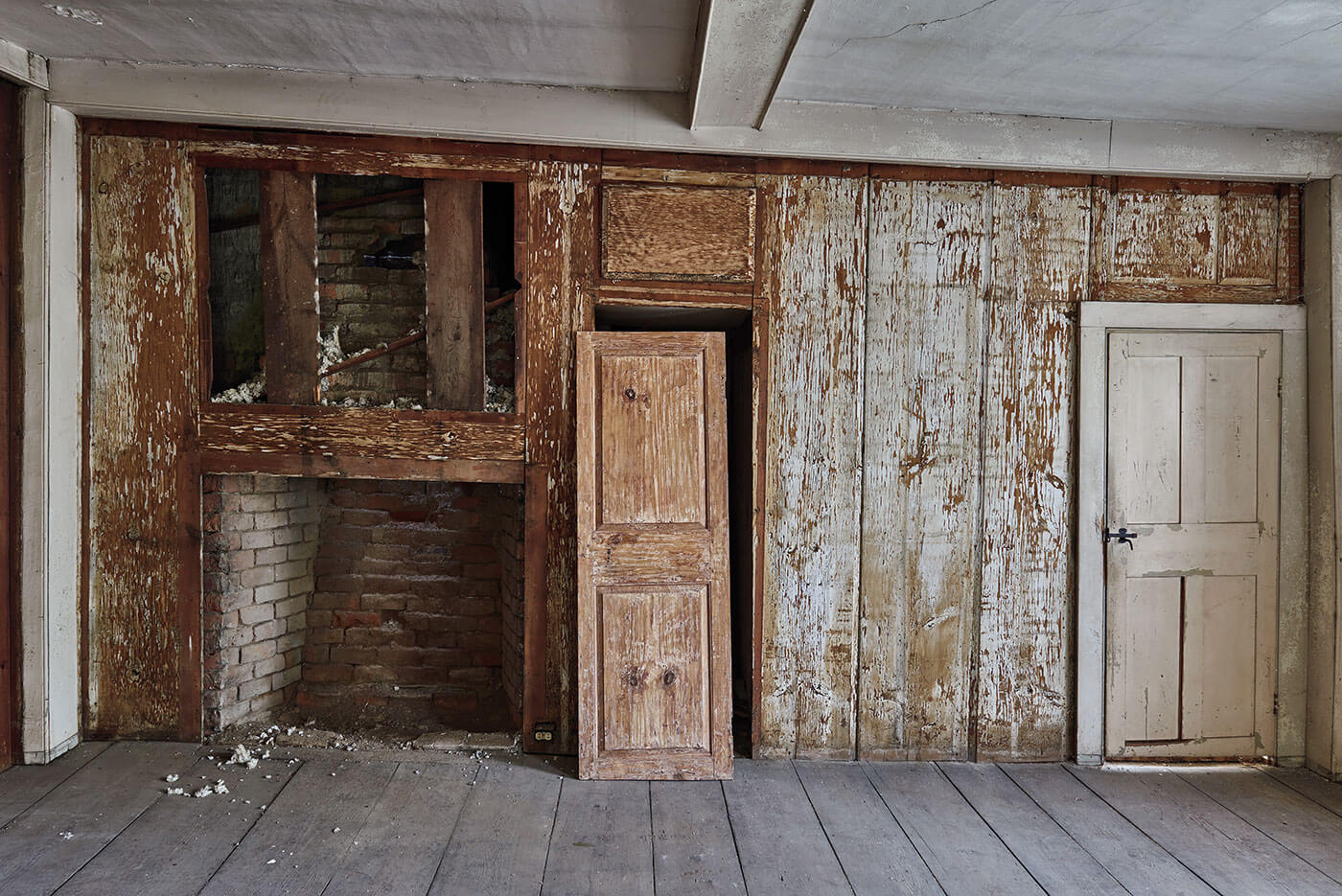 A room made of old wood waiting to be reclaimed. In the center, an antique door leans against its frame.