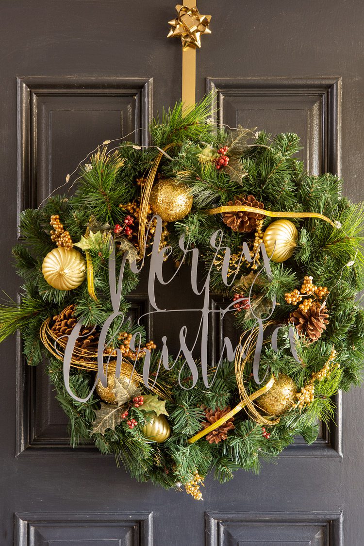 A wintergreen Christmas wreath with natural and gold accents and a "Merry Christmas" attached to the front.