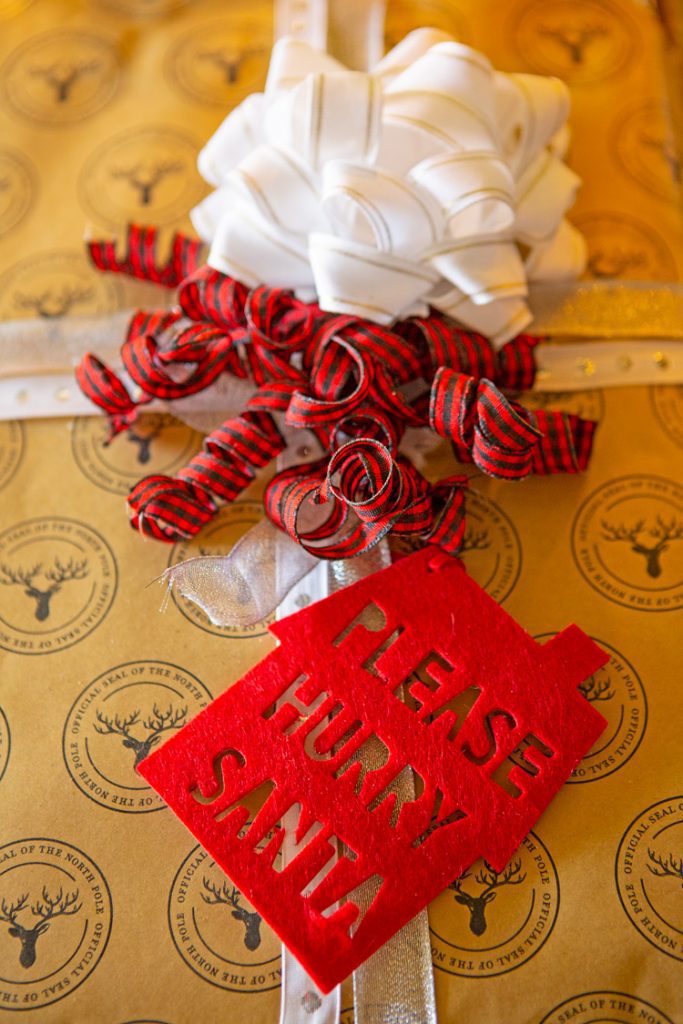Christmas cabin present with brown wrapping paper and red, gold and white ribbons with a red felt "please hurry Santa" tag attached.