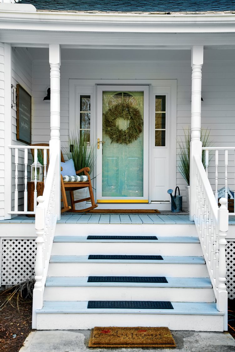 A white exterior with a sea foam green door and blue wood paneling on the floorboards of the farmhouse porch