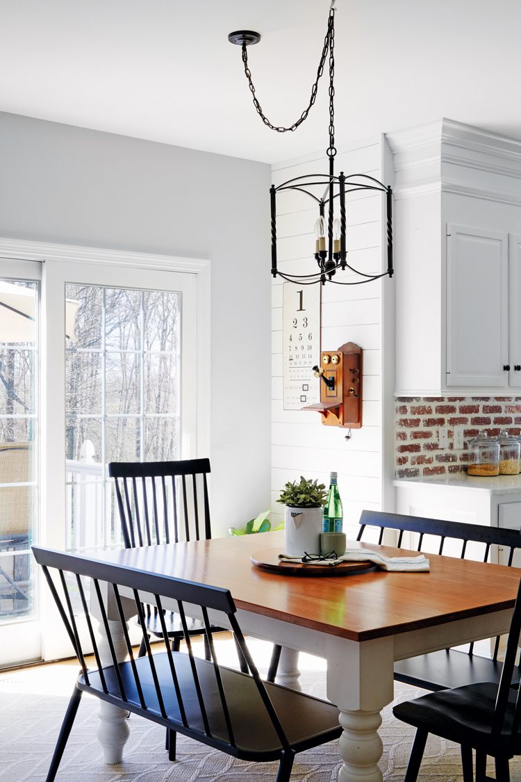 White cabinets in an exposed brick kitchen with a small kitchen table and dark chairs surrounding the table