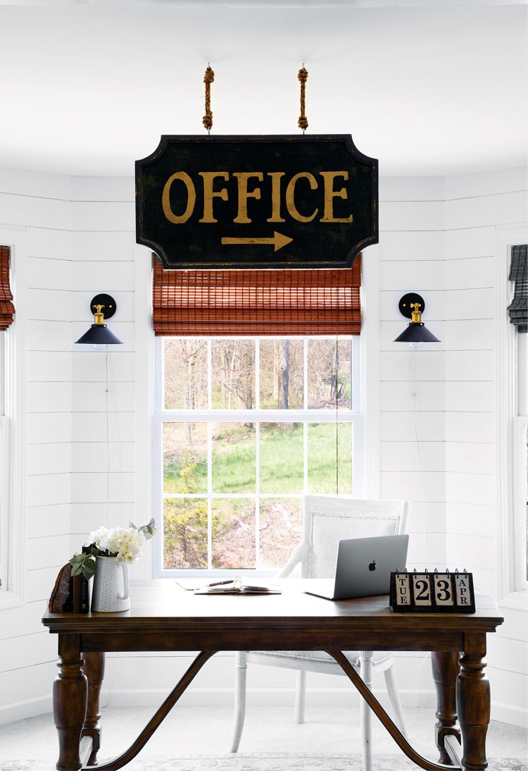 An all white office-with white chair, window frame and floor--except for the dark wood desk and silver of the apple mac