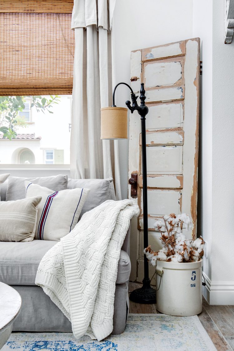 A white couch with white throw pillows in front of a white door with chippy paint