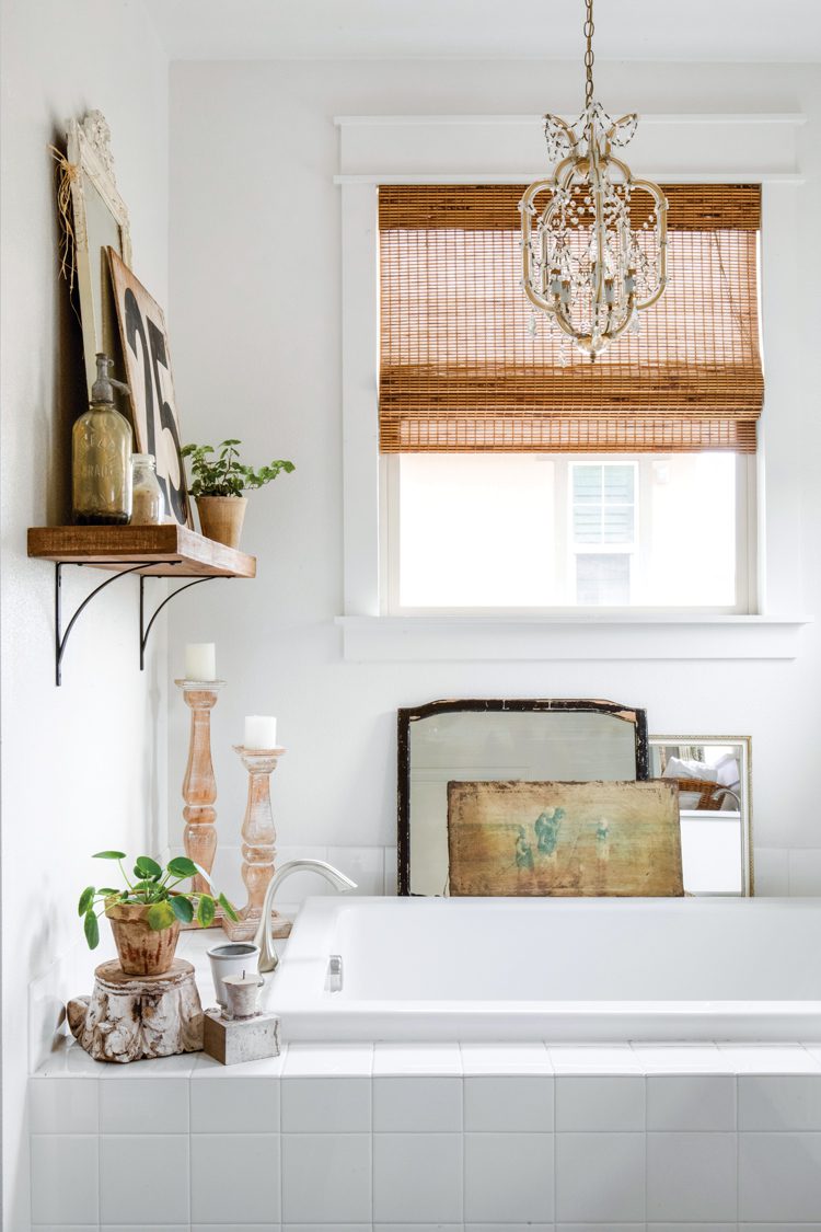 A white tile bathtub with large wood candle holders in this vintage farmhouse