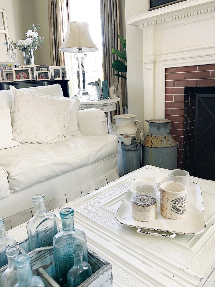 A living room table in white has several blue glass bottles and white English advertising pots