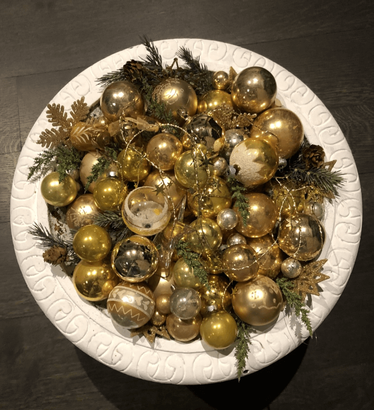 Vintage Christmas ornmanets in gold with sprigs of evergreen in a white bowl