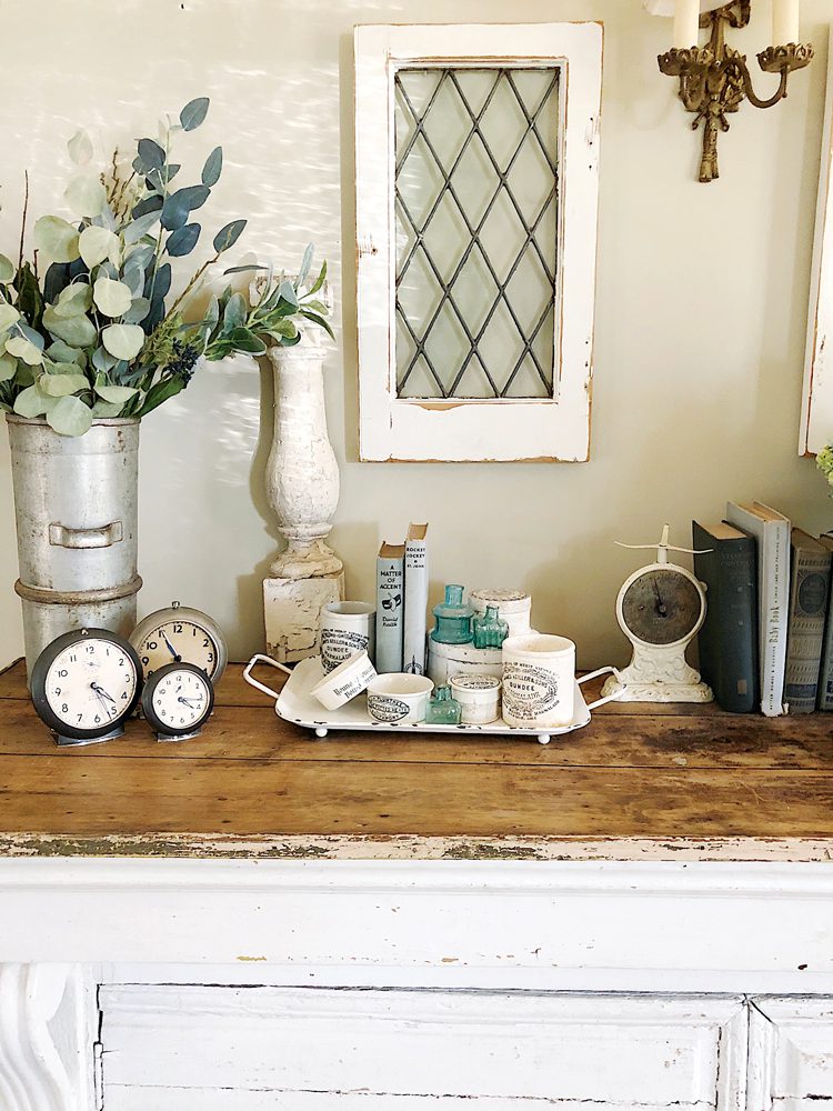 On top of a wood counter sits several white ironstone English advertising pots around a collection of antique clocks