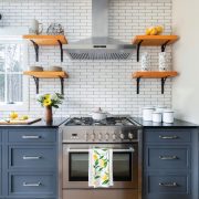 The kitchen has bluejay blue counters covered in black countertops. The white backsplash is paired with open farmhouse wood shelves