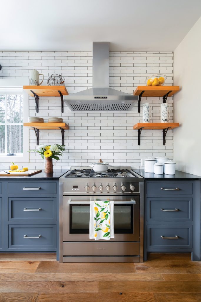 The kitchen has bluejay blue counters covered in black countertops. The white backsplash is paired with open farmhouse wood shelves