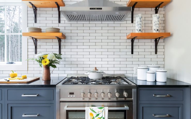 The kitchen has bluejay blue counters covered in black countertops. The white backsplash is paired with open farmhouse wood shelves