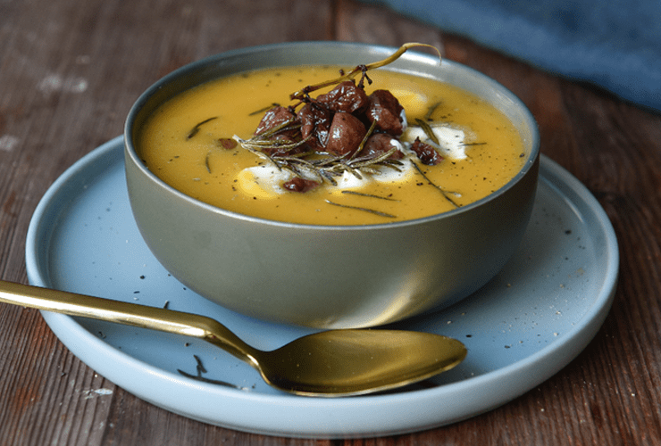 A thick yellow soup with garnishes in a gray bowl, one of our favorite farmhouse soup recipes.