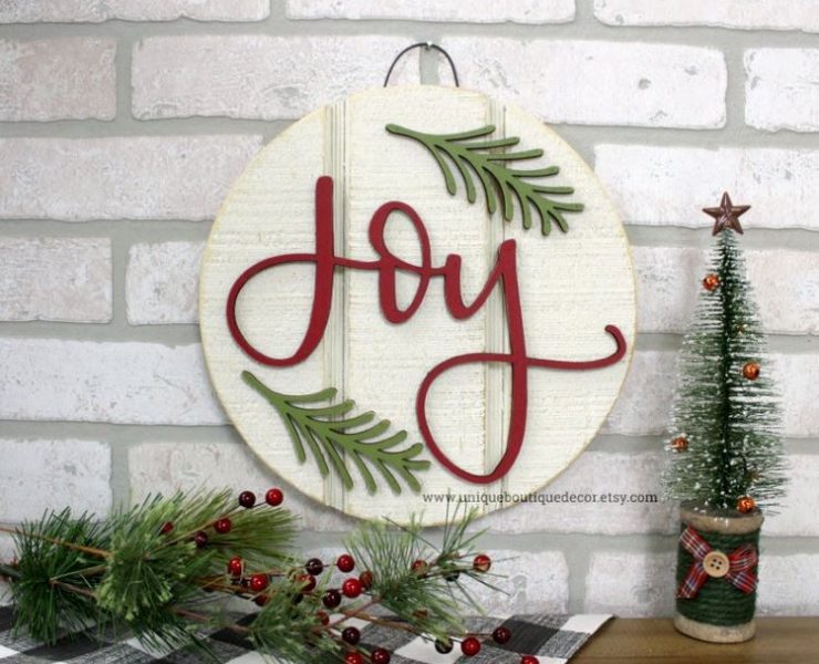 A shiplap sign that says Joy in red and evergreen sprigs