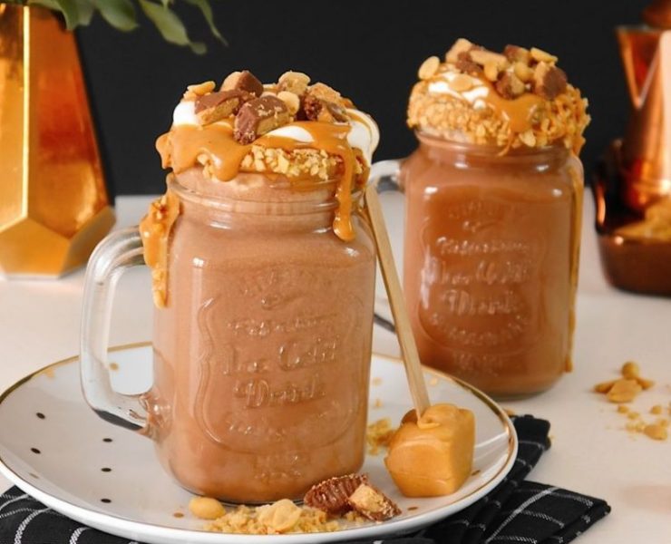 Two large glass mugs are overflowing with hot cholate mixed with peanut butter and Reese’s peanut butter cups