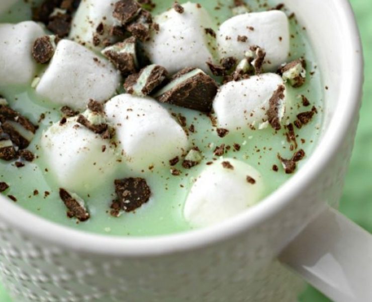 Marshmallows and pieces of mint candy are floating in a cup of mint green colored hot chocolate.