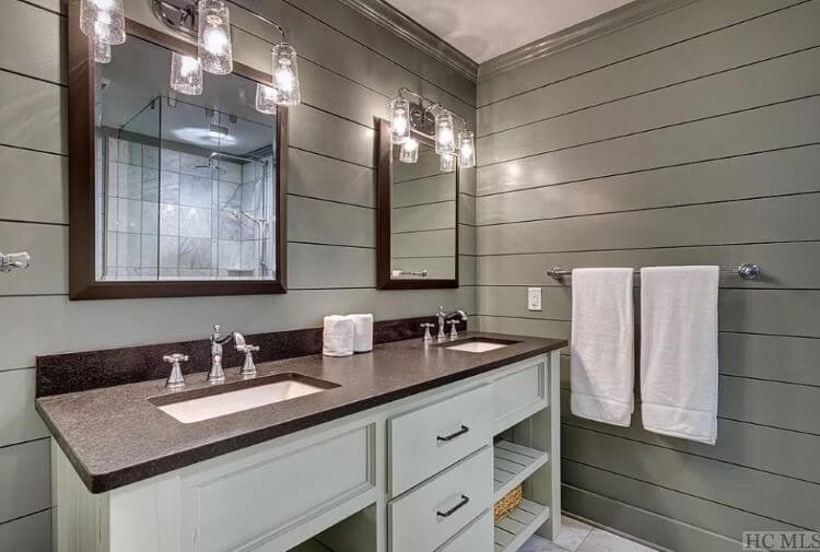 His and her matching bathroom sinks and vanity mirrors framed in dark wood and the room is paneled in grey shiplap wall paneling