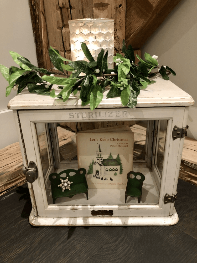 A white cabinet with antique dolls chairs inside